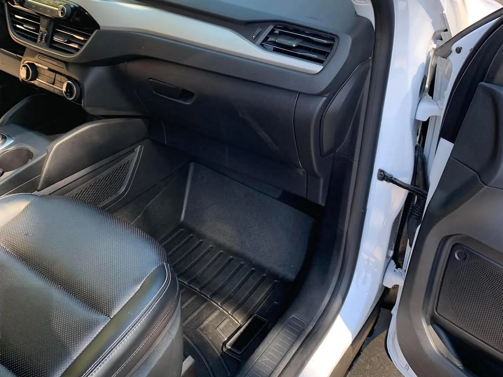 The same passenger footwell after detailing, with a clean dark floor mat and wiped-down trim