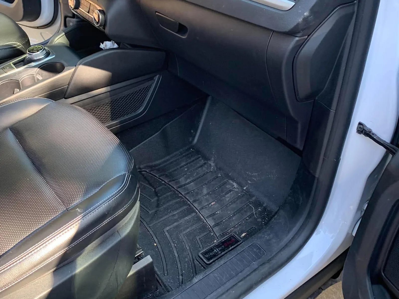 Passenger footwell of an SUV before detailing, with crumbs and dust across the rubber floor mat