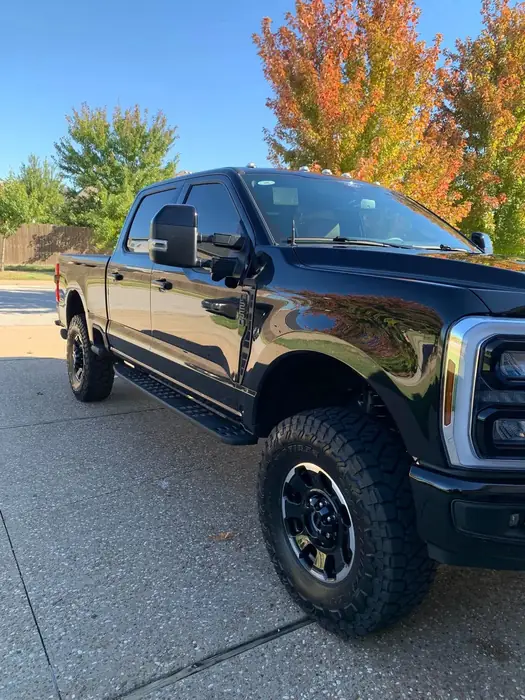 Freshly detailed black Ford pickup truck parked outdoors with autumn trees behind it