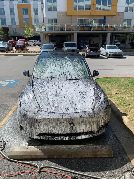 Silver car covered in wash foam on a city street